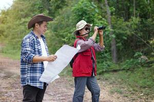 asiático mujer y hombre viajeros sostiene binocular y papel mapa a explorar natural ruta para trekking concepto, de viaje, naturaleza encuesta. al aire libre recreación actividad. aventuras estilo de vida. contento hora foto