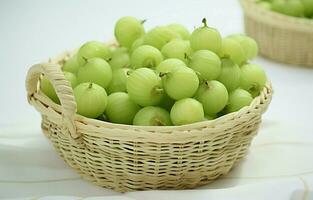 Green gooseberry in a basket on a white round wooden table, Beautiful white background. photo