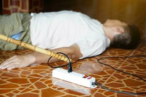 Using wooden stick is moving away the electric plug socket from the unconscious man who lay down on the floor. Concept, Electric Shock. Emergency basic rescue. First Aid photo