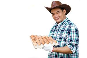 Handsome Asian man wears hat, plaid shirt, holds tray of eggs, isolated on white background. Concept, Organic agricultural farming, Farmers produce healthy eco food. Best food during bad economy. photo