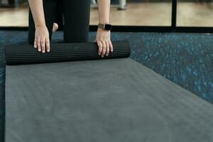 Fitness woman folding exercise mat before working out in yoga studio. rolling Yoga mat  after training healthy lifestyle photo