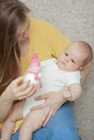 A baby boy in arms of a long haired woman looking at a toy in her hand photo