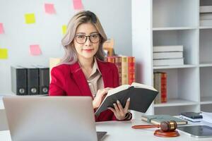 A knowledgeable and confident female lawyer working in an office with law books sitting at the table. Learn, and study, legal services, advice, justice, and real estate concepts. photo