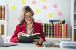 A knowledgeable and confident female lawyer working in an office with law books sitting at the table. Learn, and study, legal services, advice, justice, and real estate concepts. photo