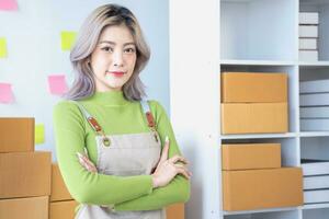 Small business entrepreneur SME, smile asian young woman, girl owner standing confident with arms crossed prepare order send to customer packing box to delivery, working online at home, ecommerce. photo