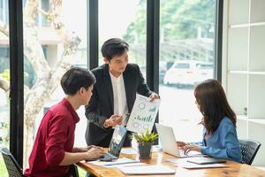 Asian business team consists of marketing staff. accountant and financial officer Help each other analyze company profits using tablets. calculator Laptop computers, graph paper, and corporate pens. photo