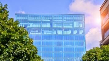 Reflection of modern commercial building on glass with sunlight. Eco architecture. Green tree and glass office building. The harmony of nature and modernity. photo