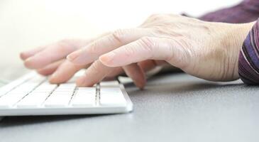 Hands of an old female typing on the keyboard, isolated on white, close-up. photo