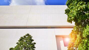 Modern white concrete building walls against blue sky. Eco architecture. Green trees and concrete office building. The harmony of nature and modernity. photo