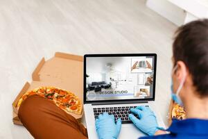 Man in medical mask and rubber gloves sits at home on a table and works with laptop during quarantine. Designer, artist, architect, businessman at remote work in a pandemic covid. Coronavirus. photo
