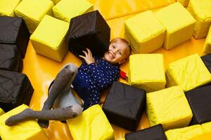 Happy laughing girl playing with toys, colorful balls in playground, ball pit, dry pool. Little cute child having fun in ball pit on birthday party in kids amusement park and play center indoor photo