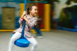 linda pequeño niña es jugando en el patio de juegos. el niña es montando en un balancearse. foto