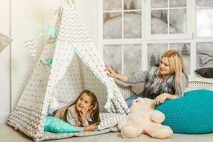 A young mother in a gray sweater and daughter are sitting in the children's room in winter. the Christmas and New Year's interior. Holiday. Family concept. photo