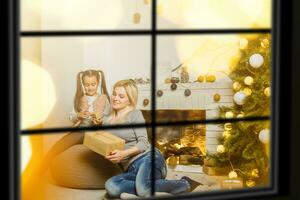 Mother and daughter sitting by a fireplace in their cozy family home enjoying winter evening through the window photo