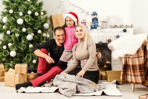 New Year. Christmas. Family. Young parents and their little daughter in Santa hats are spending time together near the Xmas tree at home photo