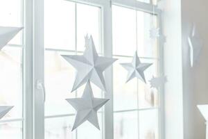 gran ventana luminosa. en el alféizar de la ventana hay una tela escocesa de punto gris con regalos y destellos con herlands. las estrellas navideñas de papel están suspendidas en el fondo de la ventana. foto