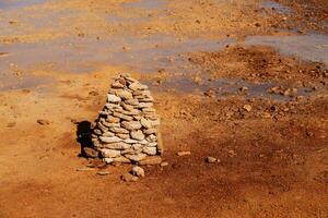 Muddy ground with spring water, with stacks of stones on one side. photo