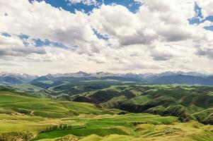 Mountain peaks and grassland are under white clouds. photo