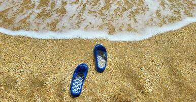 azul zapatillas en el playa en el arena en contra el antecedentes de el mar foto