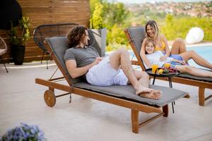 Family with a mother, father and daughter sitting on the deck chairs by the swimming pool photo