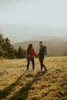 Smiling couple walking with backpacks over green hills photo