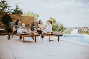 Family with a mother, father and daughter sitting on the deck chairs by the swimming pool photo