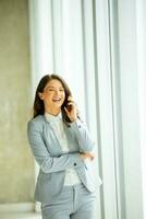 joven mujer utilizando móvil teléfono por el oficina ventana foto