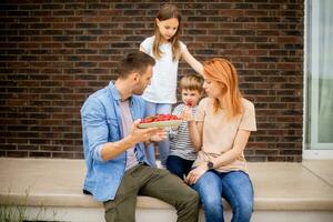 Family with a mother, father, son and daughter sitting outside on steps of a front porch of a brick house and eating strawberries photo