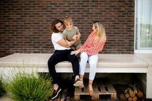 Family with a mother, father and daughter sitting outside on the steps of a front porch of a brick house photo