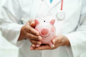 Asian woman doctor holding piggy bank, cost of treatment or education concept. photo