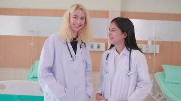 retrato do profissional médico funcionários colegas, dois uniformizado fêmea médicos falando junto, olhando às Câmera, e sorridente, feliz fisica trabalhos ocupação dentro hospital clínica. video