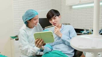 Asian female dentist explains orthodontic care work and whitening to a young male patient with teeth color shade in dental clinic, dentistry hygiene doctor, and professional healthcare in hospital. video