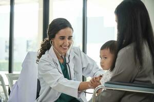 Young female pediatric doctor teases little Asian boy before medical examination at outpatient clinic hospital, people public health care checkups, and appointment visits. photo