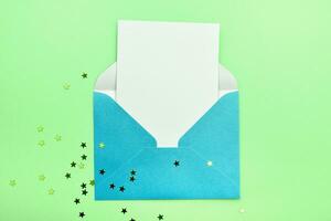 Blue open envelope with a white sheet on a green background with glitter stars. Place for your text photo