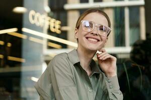 Portrait of a charming woman smiling shows her teeth in stylish glasses, coffee break. A happy manager in a shirt alone. photo