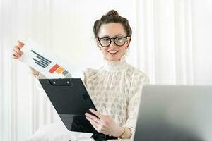A female seo specialist with glasses uses a laptop and charts. Business office clothes, jacket at the workplace. A person works in an online job. photo