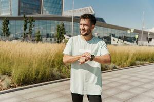 A confident male athlete trainer uses a fitness watch for cardio measurement in the app, training outside in sportswear. Healthy lifestyle and mental health. photo