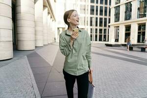 Assitstent student in a shirt going to work. Charming smiling woman goes to the office, uses the phone to message and surf. photo