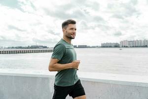 Jogging in the afternoon in the city. Runner trainer in fitness clothes T-shirt. A confident male athlete training does warm-up exercises. photo
