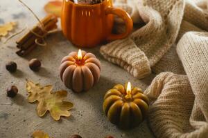 Burning candles shape of pumpking, mug with aiutumn drink, leaves and cinnamon. Autumn mood, hygge atmosphere photo