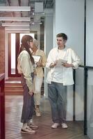 Full length photo of colleagues standing in the office corridor and talking, holding files and a notebook. Startup, coworking, management concept