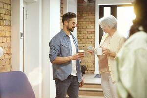 Adult woman using mobile phone while his male colleague holding coffee and standing near her in the office. Business, coworking, management concept photo