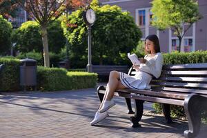 A young, stunning lady captivated by a book, seeking refuge on a park bench. The city's architecture and greenery harmoniously unite, crafting a tranquil reading haven amid the urban rush. photo