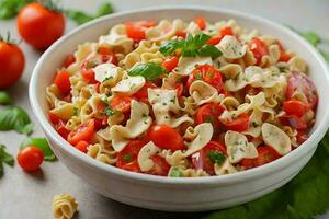 a bowl of pasta salad with farfalle pasta, cherry tomatoes, mozzarella balls, and basil leaves. photo