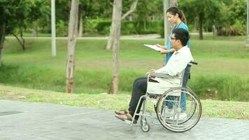 glücklich asiatisch Mann Sitzung auf Rollstuhl im das Park und nehmen Pflege durch asiatisch Krankenschwester auf Wochenenden Urlaub video