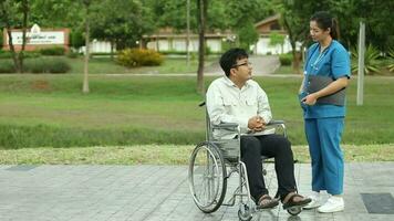 Happy Asian man sitting on wheelchair in the park and take care by asian nurse on weekends holiday video