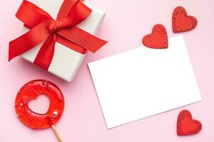 Top view photo of gift box, heart shaped lollipop on pastel pink background with copy space in the middle.