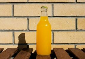 vaso limonada botella en contra el fondo de un ladrillo pared. de cerca fotografía para bandera, promoción, pintando, póster. Fresco y jugoso no alcohólico verano bebida con metal taza. foto