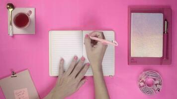 Flat lay top view of woman writing on pink background, with pink objects and pink nails video