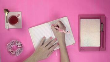 Flat lay top view of woman writing on pink background, with pink objects and pink nails video